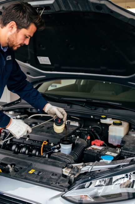 Un automobiliste vérifie le niveau d'huile et le liquide de frein d'une compacte sportive dans un garage propre, avec des pneus et une clé dynamométrique visibles.